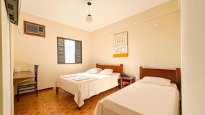 Ett hotellrum med två sängar, ett skrivbord, en stol, ett fönster med persienner och ett konstverk som hänger på väggen.