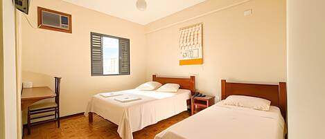 A hotel room with two beds, a desk, and a window with shutters.
