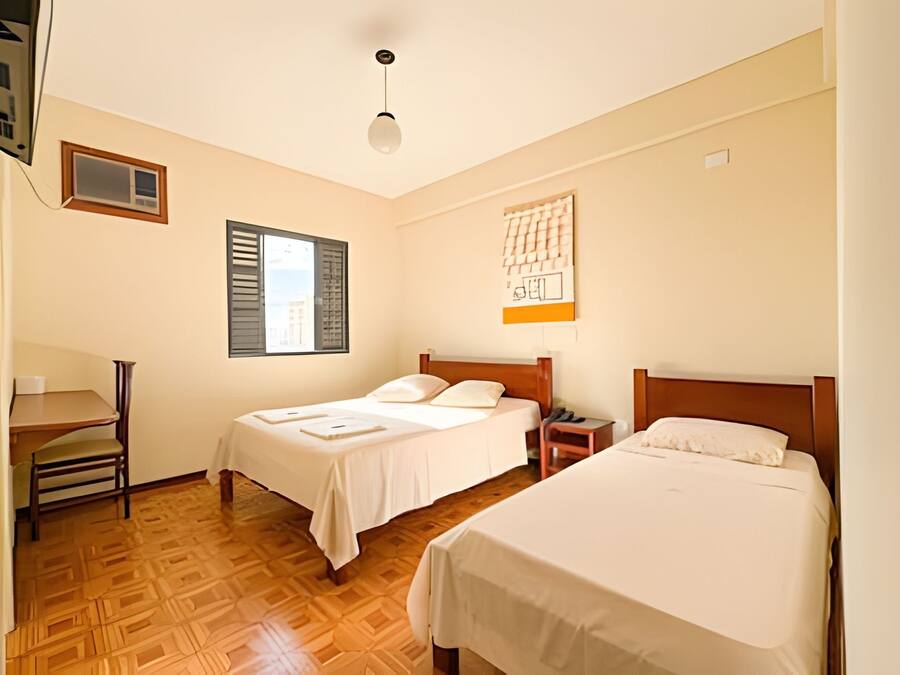 A hotel room with two beds, a desk, and a window with shutters.