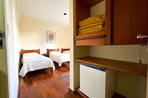 Habitación de hotel con dos camas, un refrigerador pequeño y un armario de madera con toallas.