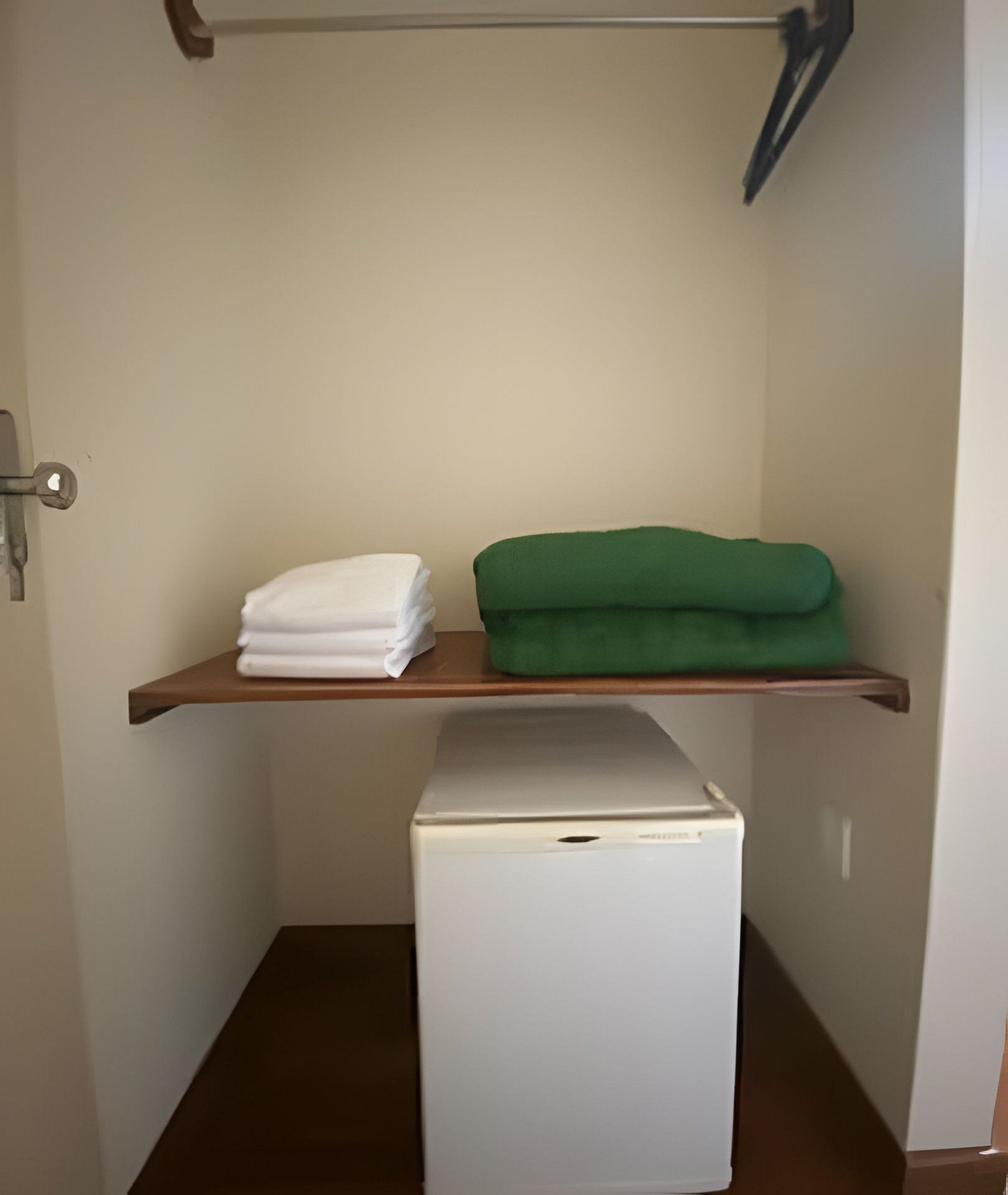 Una habitación pequeña con un refrigerador blanco, un estante de madera con toallas blancas y verdes dobladas, y una puerta con manija.