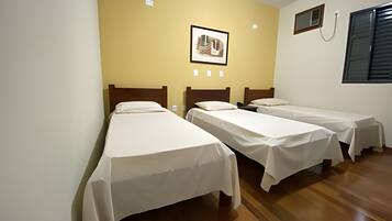 Quarto com três camas de solteiro, um quadro pendurado na parede e uma janela com persianas.