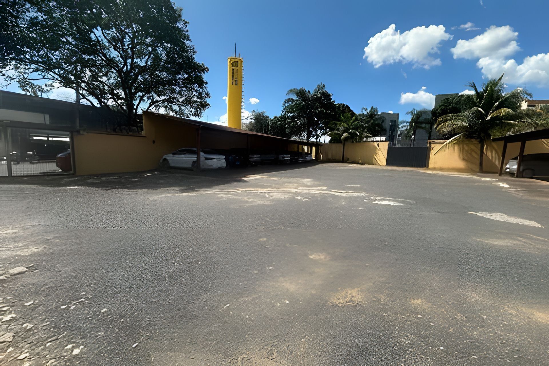 An empty parking lot with a yellow building and a tall structure in the background.