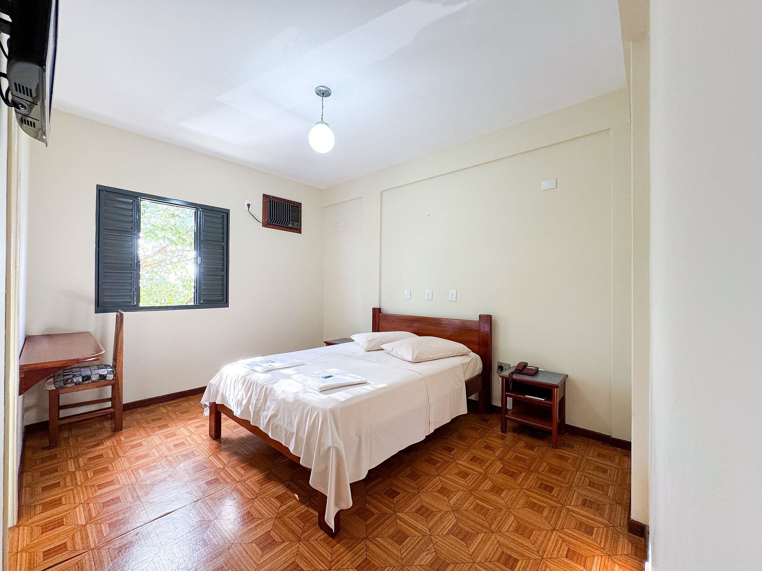 Un dormitorio con cama, mesita de noche, silla, ventana y ventilador de techo.