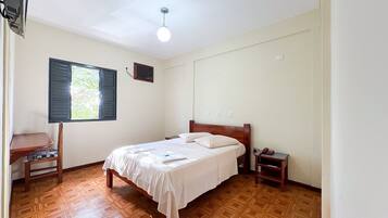 Un dormitorio con cama, mesita de noche, silla, ventana y ventilador de techo.