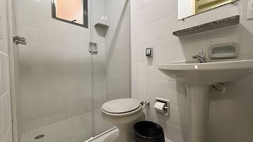 Casa de banho com sanita, lavatório, cabine de duche e um contentor de lixo.
