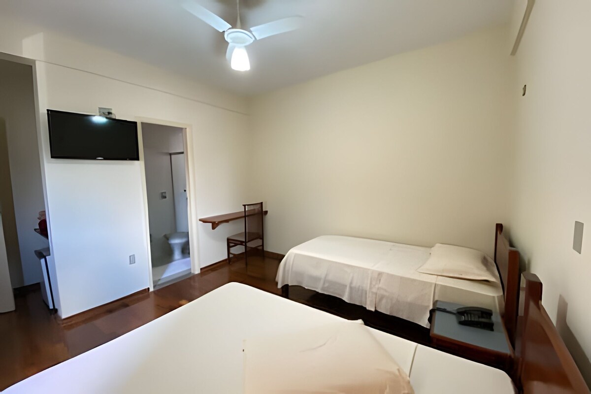 Un dormitorio con dos camas, ventilador de techo y televisión instalada en la pared.