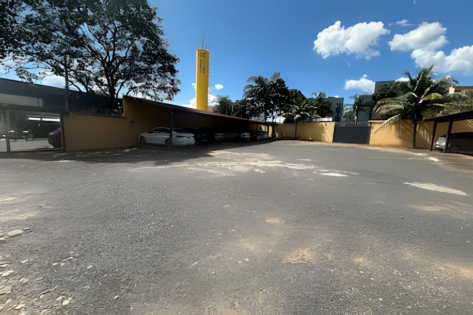 An outdoor parking area with a yellow building and a tall structure in the background.