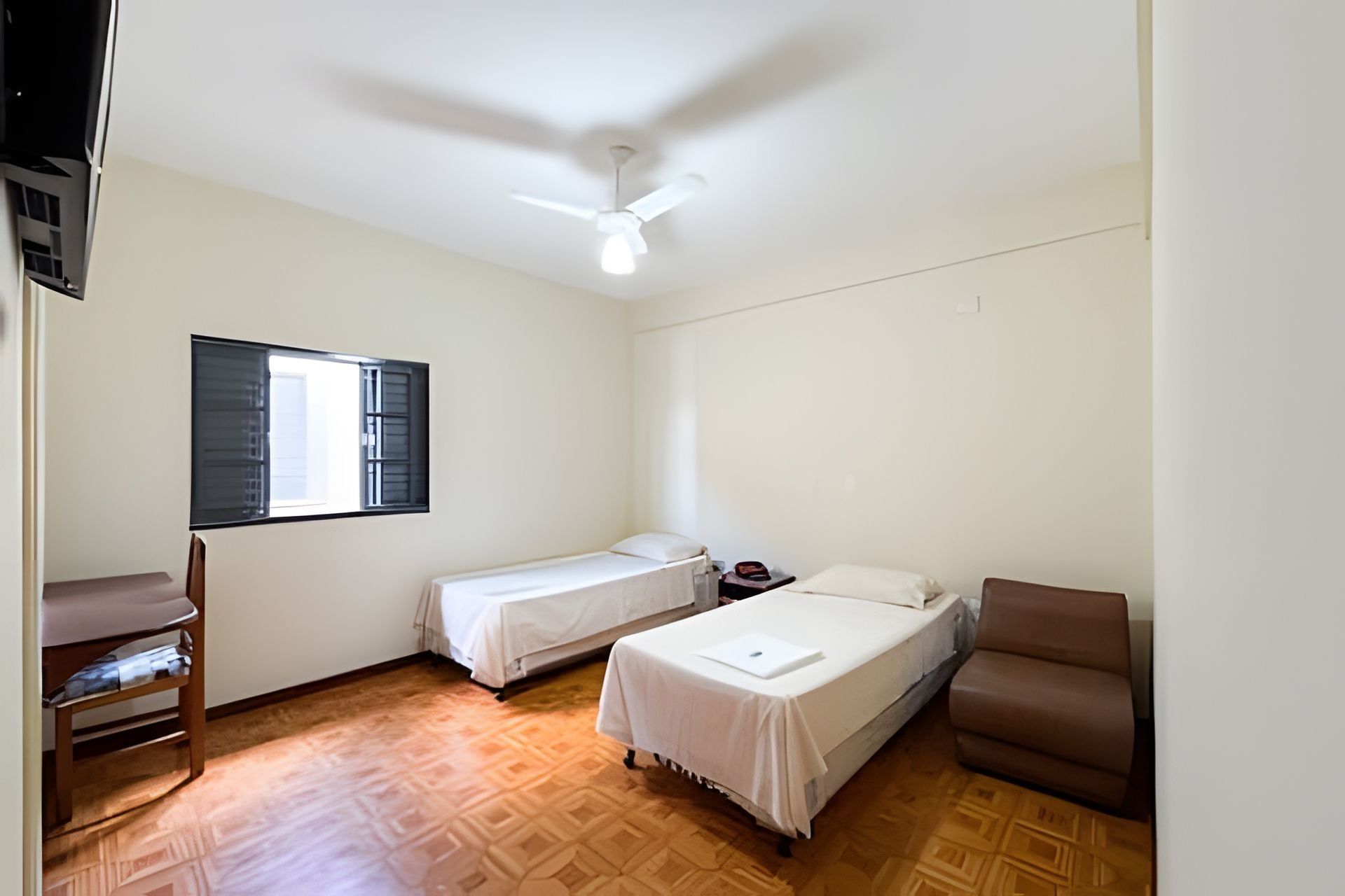 A room with two single beds, a desk, a chair, and a ceiling fan.