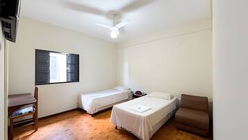A room with two single beds, a desk, a chair, and a ceiling fan.