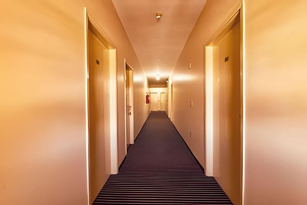 A hotel hallway with doors on both sides, a carpeted floor, and a ceiling light.