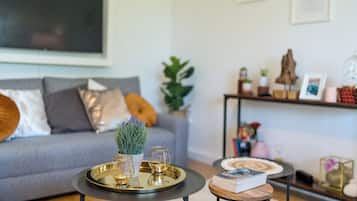 Ein modernes Wohnzimmer mit einem grauen Sofa, einem kleinen runden Tisch mit einem Buch und einer Zierpflanze.