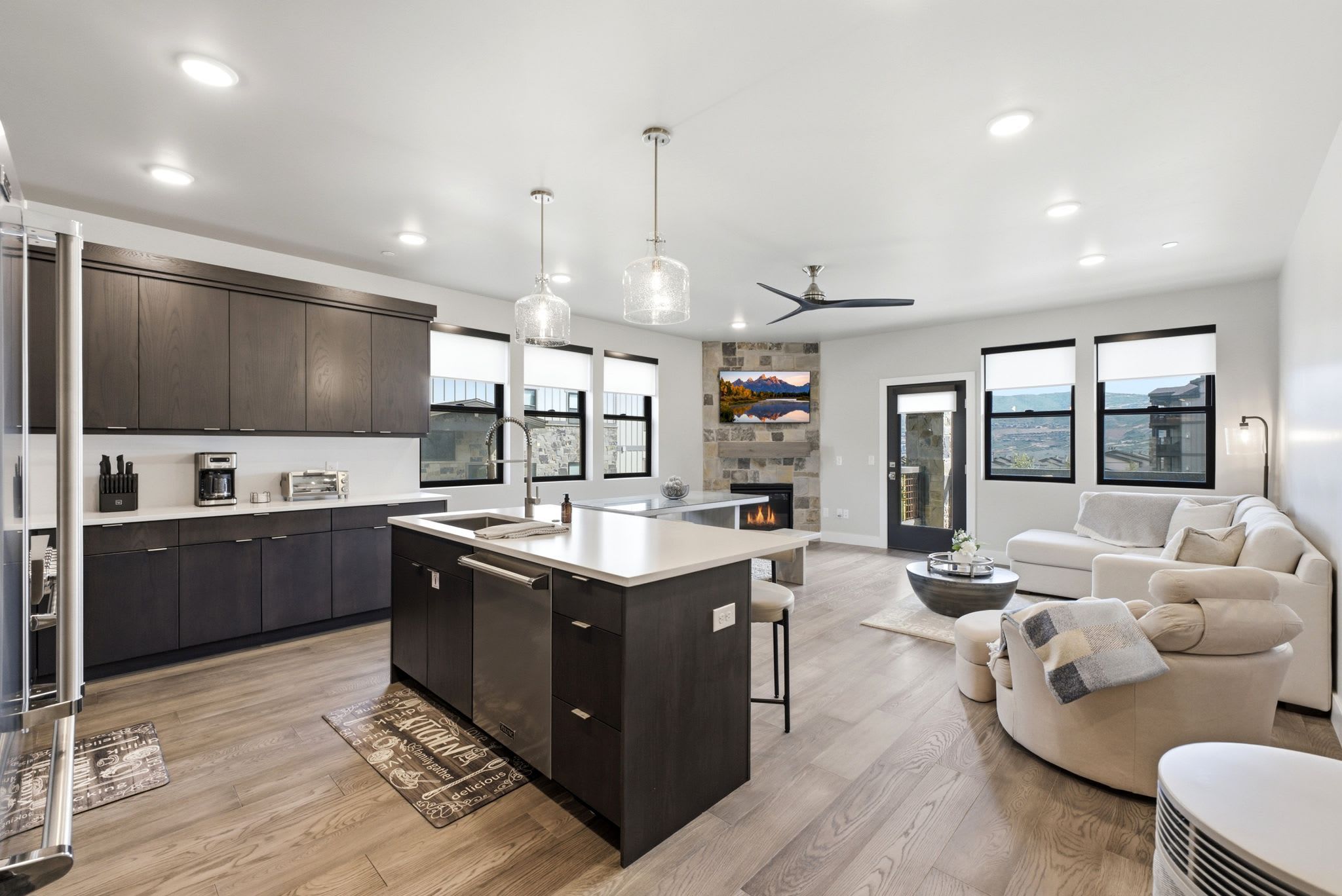 A modern kitchen with dark cabinets, a large island, and a dining area with a sofa and coffee table.