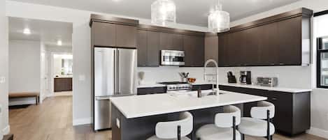 Una cocina moderna con una isla central, electrodomésticos de acero inoxidable e iluminación colgante.