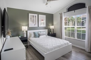 A bedroom with a bed, bedside tables, a TV, and a window with blinds. - Luxury 5BD home close to Disney with Private Pool (Kissimmee)