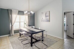 A dining area with a table, chairs, a chandelier, and a painting on the wall. - Luxury 5BD home close to Disney with Private Pool (Kissimmee)