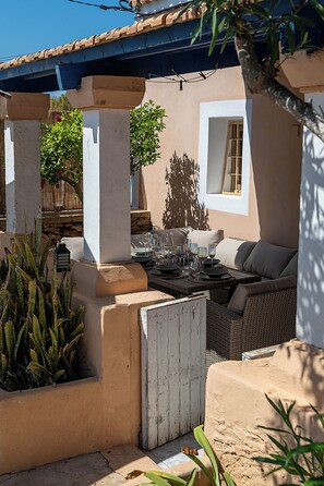 An outdoor seating area with a table set for dining, surrounded by plants and a shaded structure. - Can Llum · Mediterranean Charm in Formentera (Formentera)
