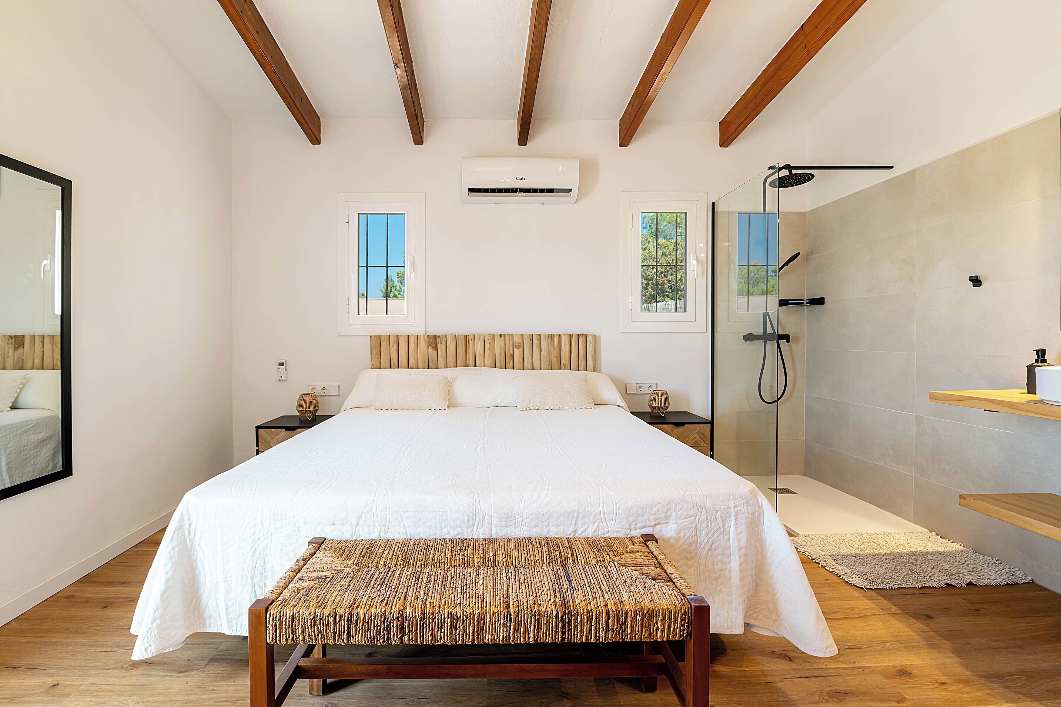 Une chambre avec un grand lit, un banc, une douche et deux fenêtres.