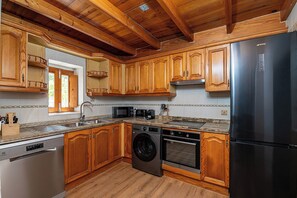 A kitchen with wooden cabinets, a stainless steel refrigerator, a dishwasher, a microwave, and a washing machine. - Can Llum · Mediterranean Charm in Formentera (Formentera)
