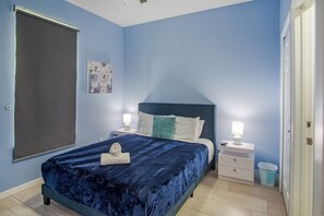 Une chambre à coucher avec un lit, des tables de chevet, une lampe fixée au mur, un tableau et une porte.