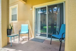 Ein überdachter Patio-Bereich mit zwei Stühlen, einem Blumentopf und einer Glastür zum Garten.