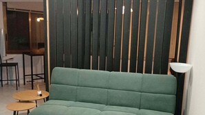 Un divano verde in una stanza con un pannello divisorio in legno a listelli, un tavolino rotondo e una lampada da terra.
