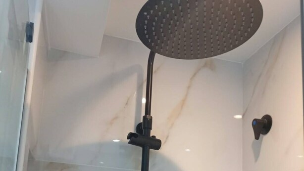 Una doccia con soffione a pioggia e doccetta manuale, una parete in marmo e un pannello comandi nero a parete.