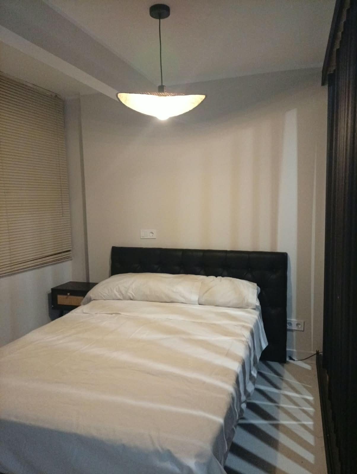 Ein Schlafzimmer mit einem Bett, einem Nachttisch, einer Steckdose und einer Deckenleuchte.