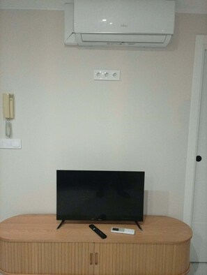 Ein Zimmer mit einem Flachbildfernseher auf einer Holzkabine, einer Fernbedienung und einem Thermostat an der Wand.