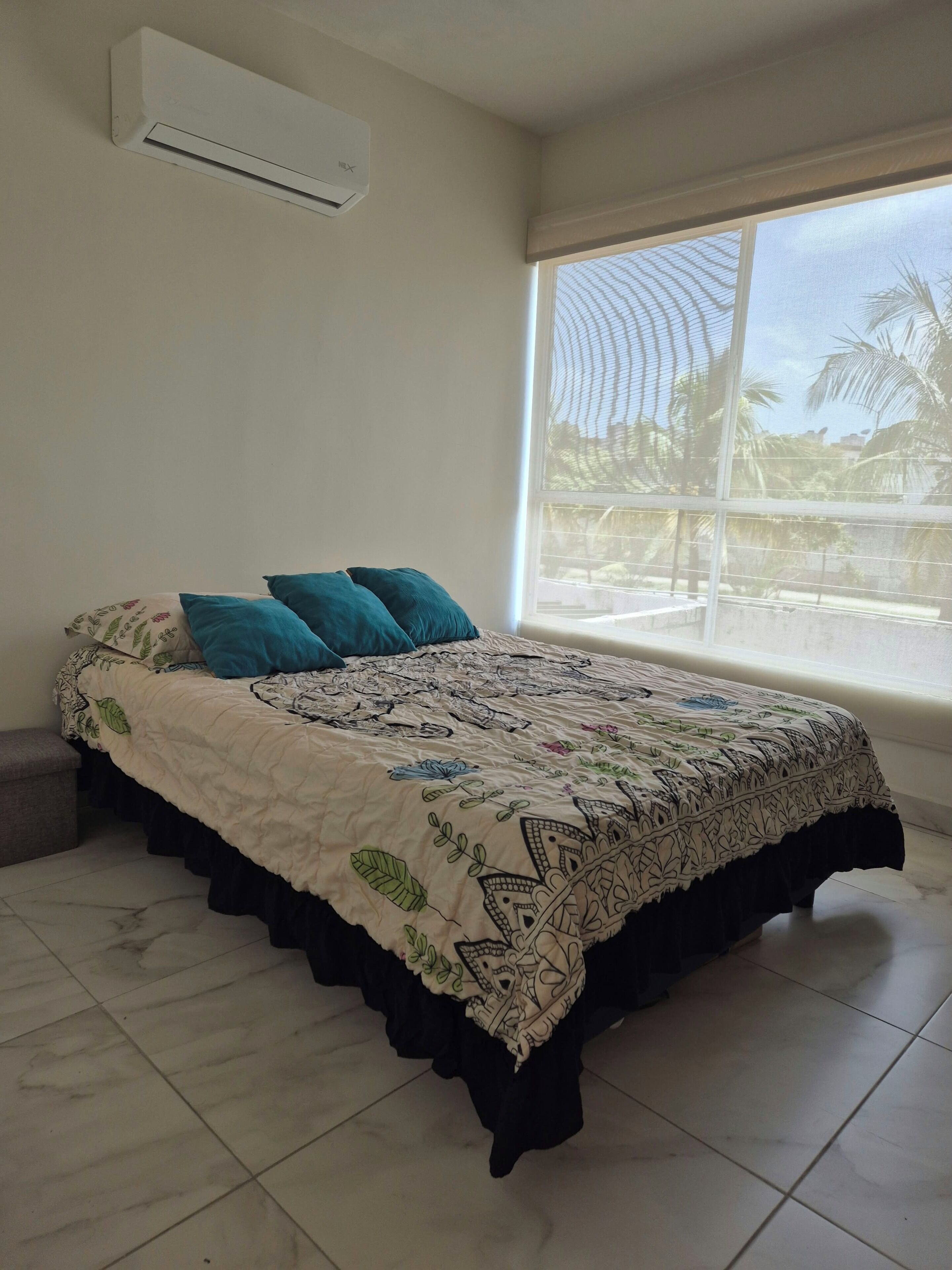 Een slaapkamer met een bed, een raam en een airconditioning.