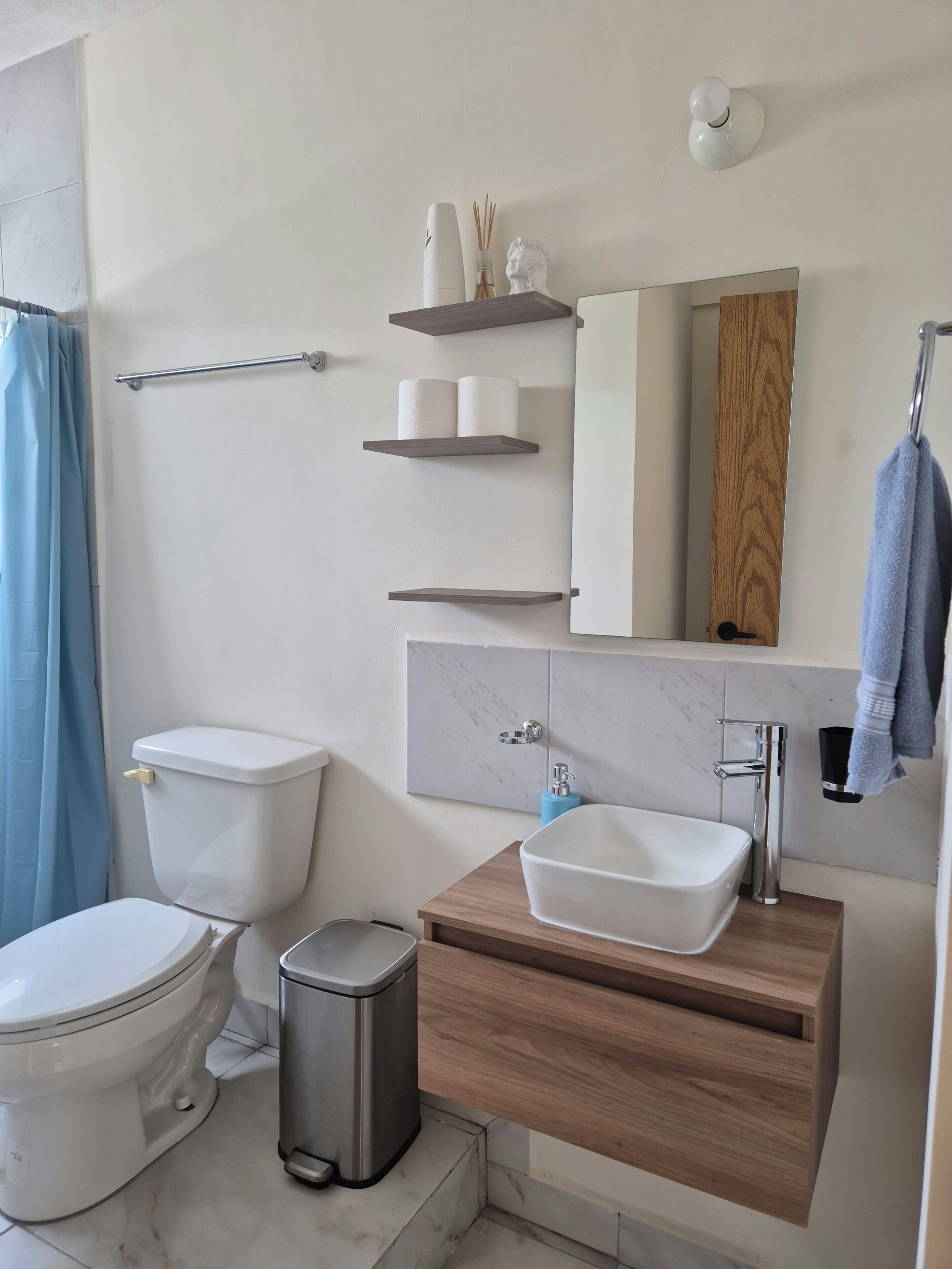 Et moderne badeværelse med toilet, bidet, skraldespand og et spejl over vasken.