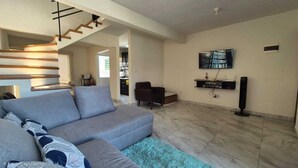 A modern living room with a grey sofa, a blue rug, a staircase, a flat-screen TV, and a sound system. - Santa Ana el Dorado (San José Novillero)