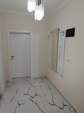 A hallway with a white door, a wall-mounted mirror, and a light fixture.
