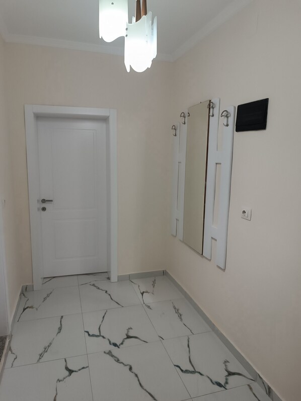 A hallway with a white door, a wall-mounted mirror, and a light fixture.
