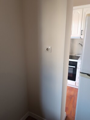 A narrow hallway with a white wall and a door leading to a kitchen area with white cabinets and a black oven.