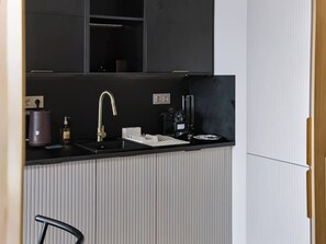 A compact kitchen with a black countertop, a stainless steel faucet, a coffee machine, and a built-in oven. - Warsaw Bemowo Apt — Parking, A/C & Balcony (Warszawa)