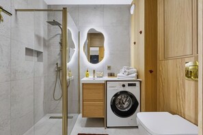 Un baño moderno con cabina de ducha de vidrio, lavadora integrada y tocador de madera.