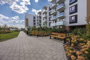 Un moderno edificio de apartamentos con un sendero pavimentado, bancos y zonas ajardinadas.