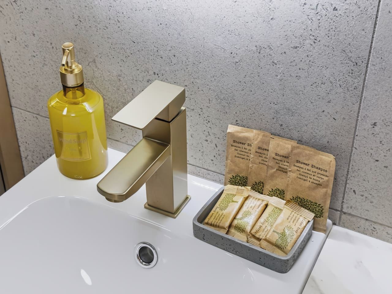 Ein Badezimmerwaschbecken mit goldenem Wasserhahn, einer gelben Flasche und einer Schale mit braunen Papiertüten mit Text.