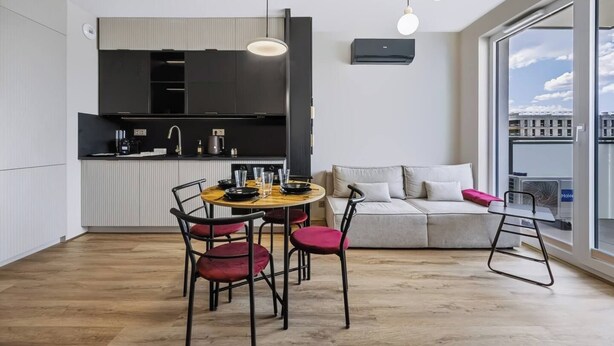 Ett modernt kök med matplats, en soffa och utsikt över staden genom stora fönster.