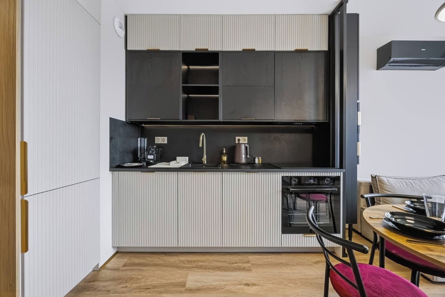 Una cocina compacta con horno integrado, un lavamanos y una zona de comedor con mesa y sillas.