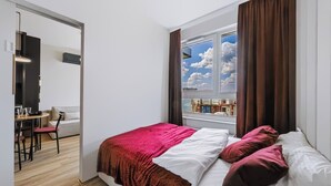 Ett modernt sovrum med en stor säng, utsikt över havet genom ett fönster och en matplats med ett bord och stolar.