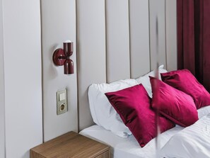 A neatly made bed with white and pink pillows, a bedside table, a wall-mounted light fixture, and a power outlet. - Warsaw Bemowo Apt — Parking, A/C & Balcony (Warszawa)
