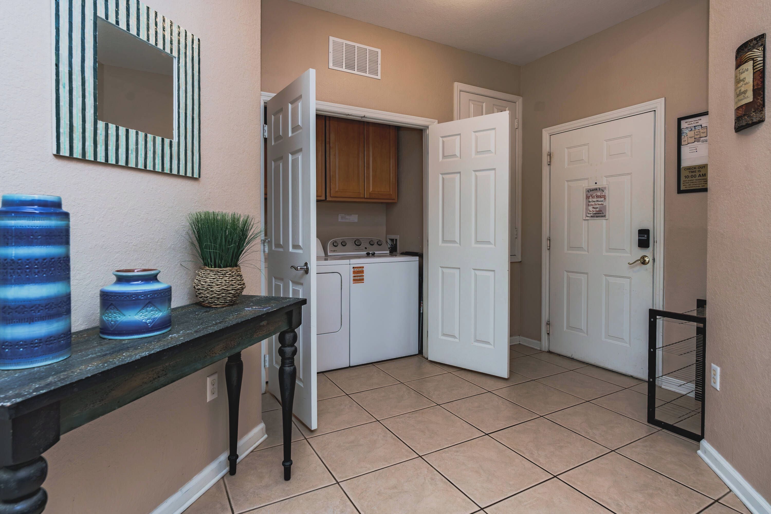 A hallway with a kitchen area, a door with a 'Thank You For Not Smoking' sign, and a check-out time sign.