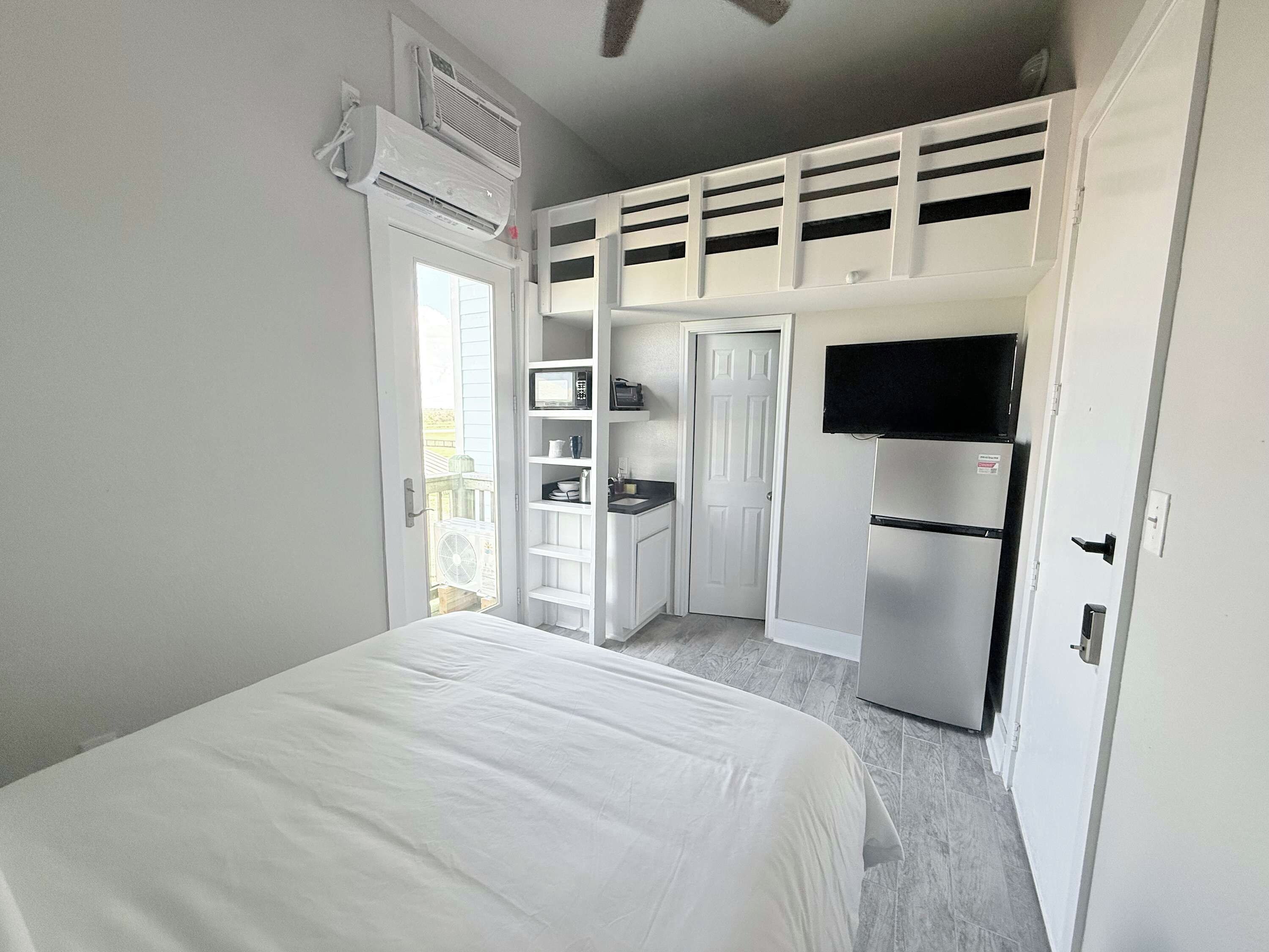 A bedroom with a bed, a kitchenette with a refrigerator, and a TV.