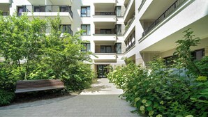 En flervåningsbyggnad med bostäder, balkonger, en stenlagd gångväg och frodig grönska.