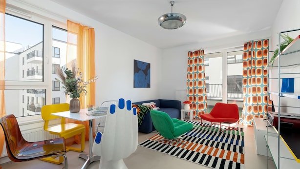 Ett modernt vardagsrum med en matplats, en soffa, en röd fåtölj, ett bord med stolar och ett stort fönster med gardiner.
