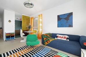 Ein modernes Wohnzimmer mit einem blauen Sofa, einem grünen Sessel und einem farbenfrohen Teppich.