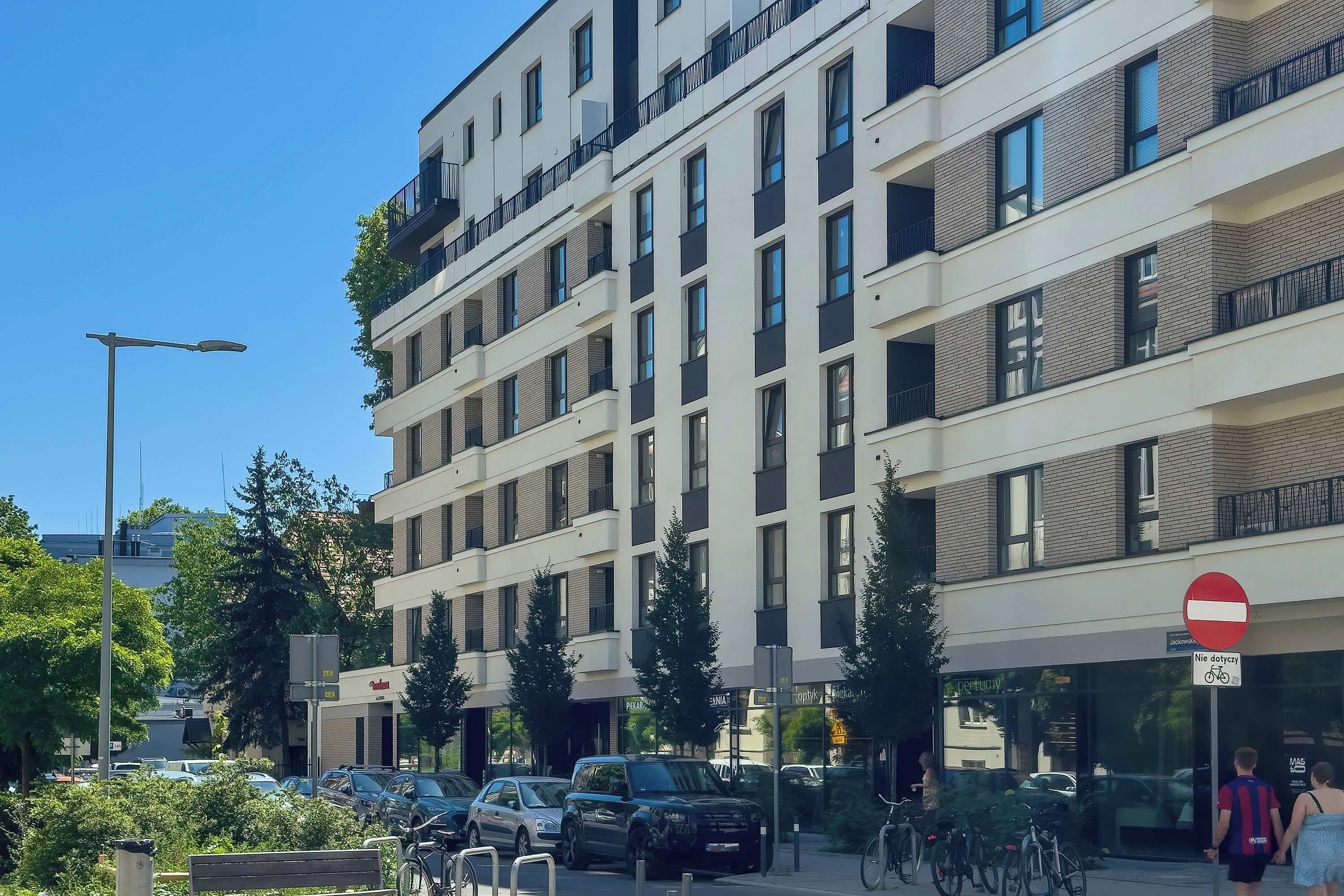 A multi-story building with a row of balconies, a no entry sign, and parked cars.
