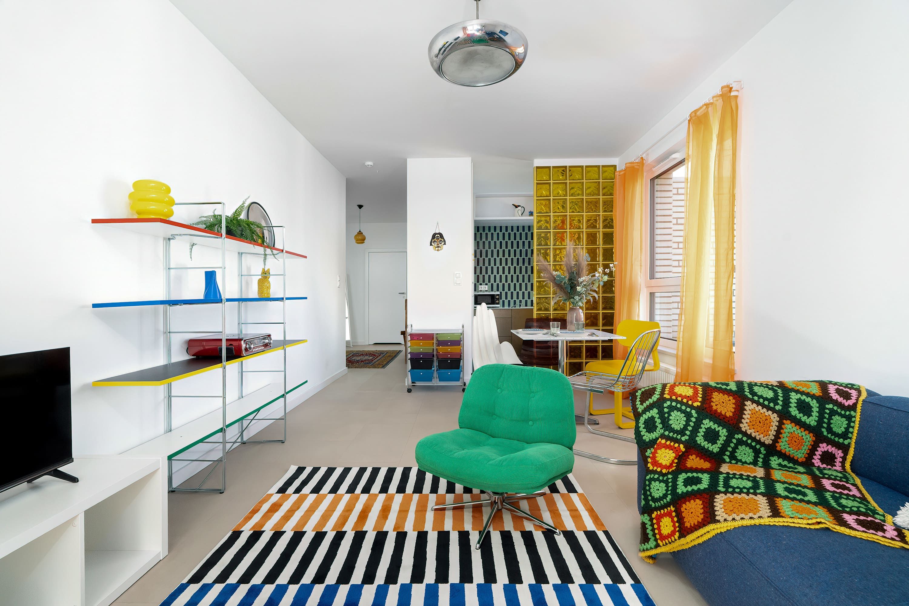 A modern living room with a green chair, a sofa, a flat-screen TV, and a striped rug.
